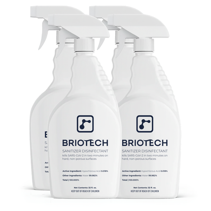 Four white spray bottles of Sanitizer Disinfectant are arranged in a staggered row. The front bottle’s label emphasizes its effectiveness against bacteria and viruses on non-porous surfaces.