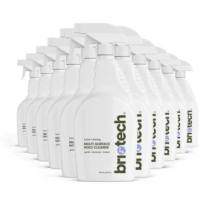 Twelve white bottles of Multi-Surface HOCl Cleaner are arranged in staggered rows, each facing forward. The bottles feature minimalist labels with green and blue text, emphasizing that this deodorizing multi-surface cleaner is safe for kids and pets.