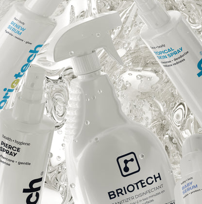 The Home + Skin Refill Bundle consisting of four white spray bottles labeled for skin serum, topical skin spray, piercing spray, and sanitizer disinfectant, set against a background of swirling water.